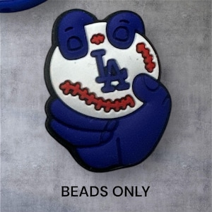May include: A blue and white baseball-themed bead with the letters "LA" on a white baseball. The bead is held in a blue hand and has red stitching. The text "BEADS ONLY" is at the bottom.