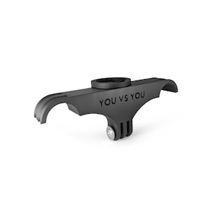 Puede incluir: Un soporte de manillar de bicicleta en color negro mate con una interfaz superior circular y un adaptador de tres puntas orientado hacia abajo con un perno de metal plateado. El lateral del soporte tiene grabado el texto YOU VS YOU.