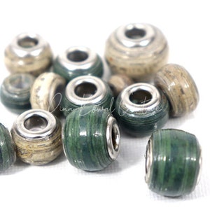 Pu&ograve; includere: Una collezione di perline di carta verde e beige con accenti metallici argentati. Le perline sono rotonde e hanno un foro al centro per essere infilate.