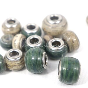 Pu&ograve; includere: Primo piano di un gruppo di perline di carta verde e beige con accenti metallici argentati. Le perline sono rotonde e hanno una superficie testurizzata.