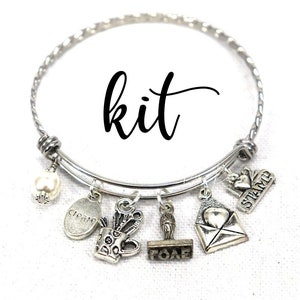 May include: A silver charm bracelet with the word "kit" written on it. The bracelet has several charms including a pearl, a stamp, an envelope, a mug, a quill pen, and a stamp with the word "FOAF" on it.