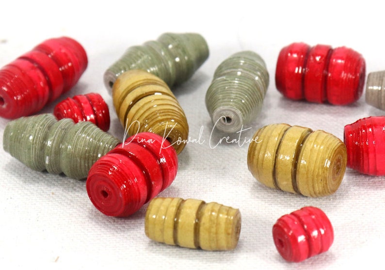 May include: A collection of colorful paper beads in red, beige, and green. The beads are made of rolled paper and have a spiral design.