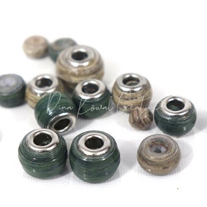 Pu&ograve; includere: Una collezione di perline di carta verde e marrone con accenti metallici argentati. Le perline sono rotonde e hanno un foro al centro per essere infilate.