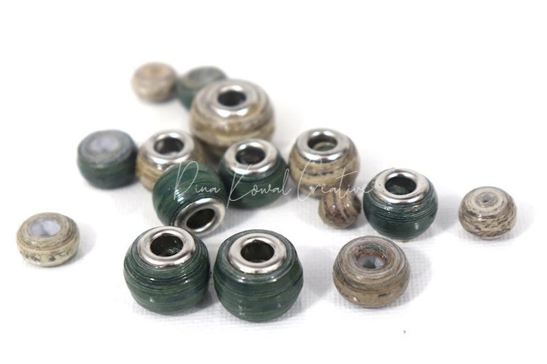 Pu&ograve; includere: Una collezione di perline di carta verde e marrone con accenti metallici argentati. Le perline sono rotonde e hanno un foro al centro per essere infilate.