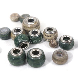 Pu&ograve; includere: Una collezione di perline di carta verde e marrone con accenti metallici argentati. Le perline sono rotonde e hanno un foro al centro per essere infilate.