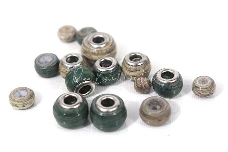 Pu&ograve; includere: Una collezione di perline di carta verde e marrone con accenti metallici argentati. Le perline sono rotonde e hanno un foro al centro per essere infilate.