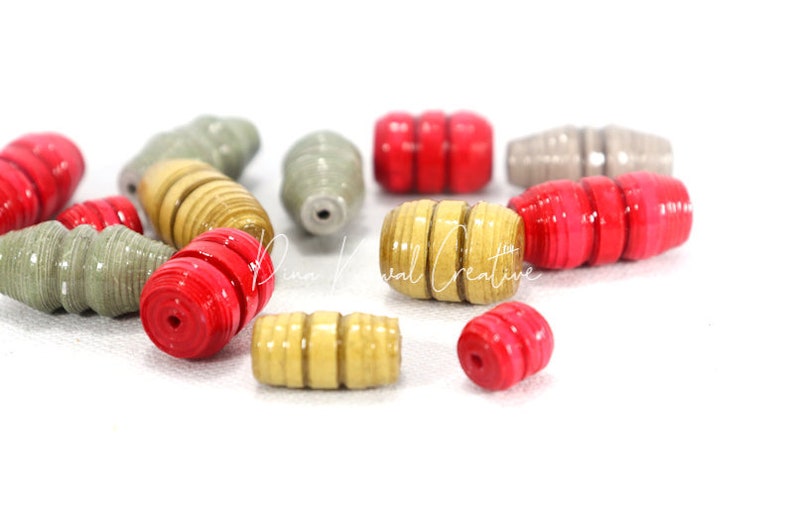 May include: A collection of colorful paper beads in red, gold, and gray. The beads are made of rolled paper and have a unique, textured look.
