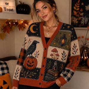 May include: A long-sleeve V-neck cardigan featuring a patchwork design with Halloween motifs including a black raven, a jack-o'-lantern, mushrooms, a lantern, and books. The knit fabric incorporates black, orange, and cream colors with a button front.