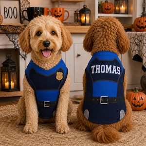 May include: A dog wearing a blue and dark blue police officer costume vest. The front features a gold badge emblem. The back displays the name THOMAS in white capital letters above a printed black belt with a silver buckle and silver accents.