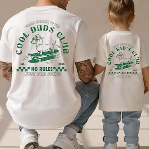 Pode incluir: Camisetas brancas com gráficos correspondentes. A camisa adulta mostra um dachshund em um skate e o texto "Cool Dads Club" e "No Rules Just Dad Jokes". A camisa infantil diz "Cool Kid's Club" e "No Rules Just Fun".