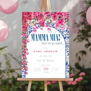 Op de afbeelding: Een babyborrelbord op een houten ezel. Het bord bevat de woorden "MAMMA MIA!" en "here we go again..." in blauw, met roze bloemaccenten. Het bord bevat ook de tekst "THE BABY SHOWER" en de namen "Liv & Dave".