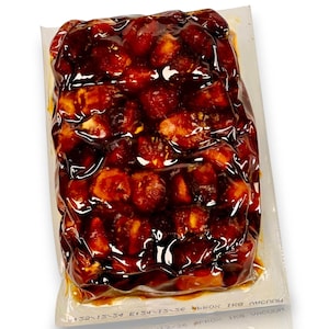 May include: A vacuum-sealed package filled with a dark, glossy food product. The contents appear to be small, round, and reddish-brown, possibly fruits or vegetables, coated in a shiny sauce. The packaging is transparent, allowing a clear view of the contents.