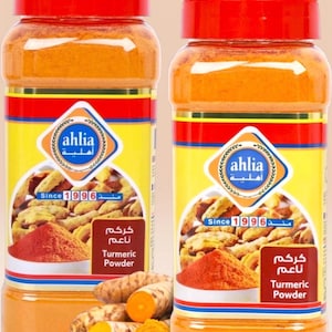 May include: Two clear plastic jars of turmeric powder with red lids. The jars have yellow and white labels with the brand name "ahlia" and the text "Turmeric Powder". The image also shows turmeric roots and powder.