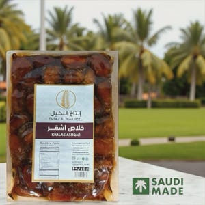 May include: A clear plastic package filled with Khalas Ashqar dates. The label reads "ENTAJ AL NAKHEEL" and "KHALAS ASHQAR". The background features palm trees and a grassy area, with a "SAUDI MADE" logo.