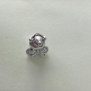 May include: A small, silver-colored charm in the shape of a cartoon dog with a bow tie. The charm has a detailed design, including the dog's face, ears, and bow. The charm is likely made of metal and is suitable for jewelry making or as a decorative element.