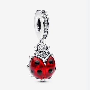 Peut inclure: Un charm en argent en forme de coccinelle avec un corps rouge translucide orné de points noirs. La tête de la coccinelle est incrustée de petites pierres claires, et la bélière est également décorée d'une rangée de pierres claires sur le bord.