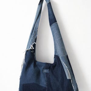 以下が含まれることがあります： パッチワークデザインのデニムトートバッグ。バッグは、さまざまなブルーデニムの色合いで、大きなポケットと長いストラップが付いています。「LULA」の文字がバッグの前面に見えます。