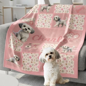 May include: A soft pink throw blanket featuring a repeating grid pattern of white puppies, paw prints, and grooming accessories. The blanket displays the name Charlie in cursive script and includes illustrations of bones and hearts.