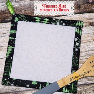 Puede incluir: Un posavasos acolchado blanco con un borde negro y verde con un diseño de árbol de Navidad y copo de nieve. El posavasos mide 9 pulgadas por 9 pulgadas. El texto "Finished Size 9 inches x 9 inches" está impreso en un rectángulo rojo.
