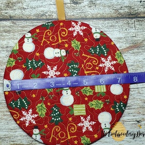 K&ouml;nnte beinhalten: Ein runder, roter Weihnachtsschmuck mit einem festlichen Muster mit Schneem&auml;nnern, Schneeflocken und Stechpalmen. Der Schmuck hat einen Durchmesser von etwa 18 cm und ein goldenes Band zum Aufh&auml;ngen. Das Design beinhaltet das Wort "JOY".