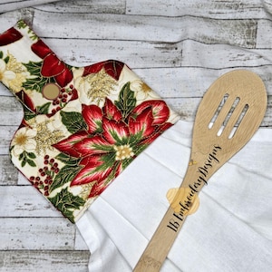 May include: A festive kitchen towel holder featuring a poinsettia design in red, green, and gold, attached to a white towel. A wooden slotted spoon with the text "IB Embroidery Designs" is also visible.