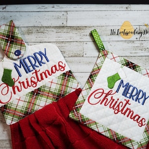 May include: Two Christmas-themed kitchen towels with a green, red and white plaid pattern. One towel is a dish towel with a hanging loop and the other is a pot holder. Both towels have the text "Merry Christmas" embroidered in red and blue with a green stocking.