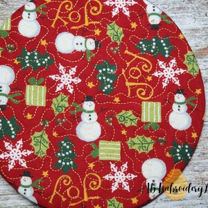 K&ouml;nnte beinhalten: Ein runder, roter Weihnachtsstoff mit einem sich wiederholenden Muster aus Schneem&auml;nnern, Schneeflocken, gr&uuml;nen Weihnachtsb&auml;umen und verpackten Geschenken. Das Design enth&auml;lt das Wort "JOY" und ist mit goldenem Faden gen&auml;ht. Das Design stammt von "IB Embroidery Designs."
