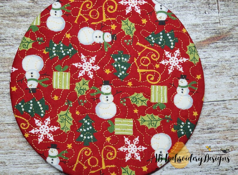 K&ouml;nnte beinhalten: Ein runder, roter Weihnachtsstoff mit einem sich wiederholenden Muster aus Schneem&auml;nnern, Schneeflocken, gr&uuml;nen Weihnachtsb&auml;umen und verpackten Geschenken. Das Design enth&auml;lt das Wort "JOY" und ist mit goldenem Faden gen&auml;ht. Das Design stammt von "IB Embroidery Designs."