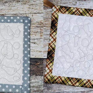 Pode incluir: Dois pegadores de panela acolchoados com fundo branco e um desenho de vários animais e círculos. Um pegador tem uma borda de tecido de bolinhas cinza e branco e o outro tem uma borda de tecido xadrez marrom e verde.