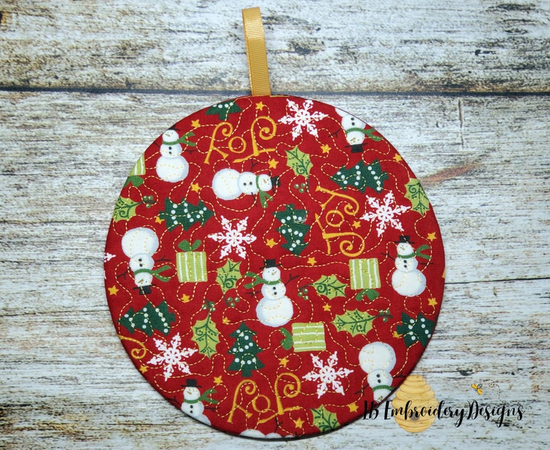 K&ouml;nnte beinhalten: Ein runder, roter Weihnachtsschmuck mit einem goldenen Band zum Aufh&auml;ngen. Das Ornament zeigt ein sich wiederholendes Muster aus Schneem&auml;nnern, Schneeflocken, Weihnachtsb&auml;umen und Geschenkboxen. Das Wort "JOY" ist ebenfalls enthalten.