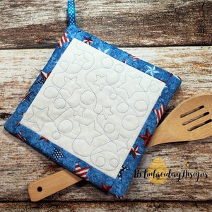 May include: A blue and red fabric pot holder with a white center featuring a quilted design of stars and circles. The pot holder has a blue ribbon loop for hanging. The pot holder is on a wooden surface with a wooden spoon.