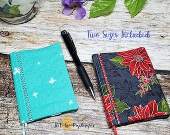 May include: Two fabric notebook covers in different sizes and patterns. The smaller cover is turquoise with a white butterfly pattern. The larger cover is dark blue with a red poinsettia pattern. Both covers have a red ribbon bookmark.
