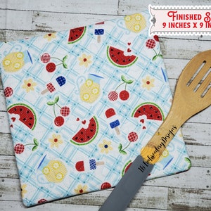 May include: A white cotton pot holder with a summer picnic theme. The design features watermelon slices, cherries, lemonade pitchers, and popsicles on a blue and white checkered background. The pot holder measures 9 inches by 9 inches. The text "Finished Size 9 inches x 9 inches" is visible in the upper right corner of the image.