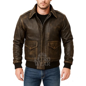 Könnte beinhalten: Braune Lederjacke im Used-Look mit Kragen und zwei Vordertaschen. Die Jacke hat einen Reißverschluss und schwarze gerippte Bündchen und Saum. Getragen über einem schwarzen Shirt und blauen Jeans.