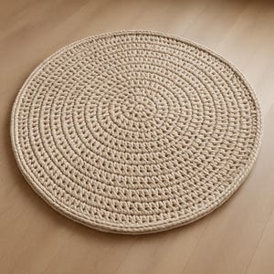 May include: A round, beige crocheted rug with a circular pattern. The rug is made of thick yarn and has a soft, textured surface.