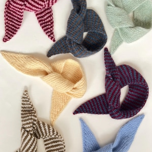 Può includere: Una collezione di sciarpe lavorate a maglia a mano in vari colori, tra cui rosa, blu, giallo e verde. Alcune sciarpe hanno motivi a righe, mentre altre sono a tinta unita. Le sciarpe sono annodate al centro, creando un design unico.