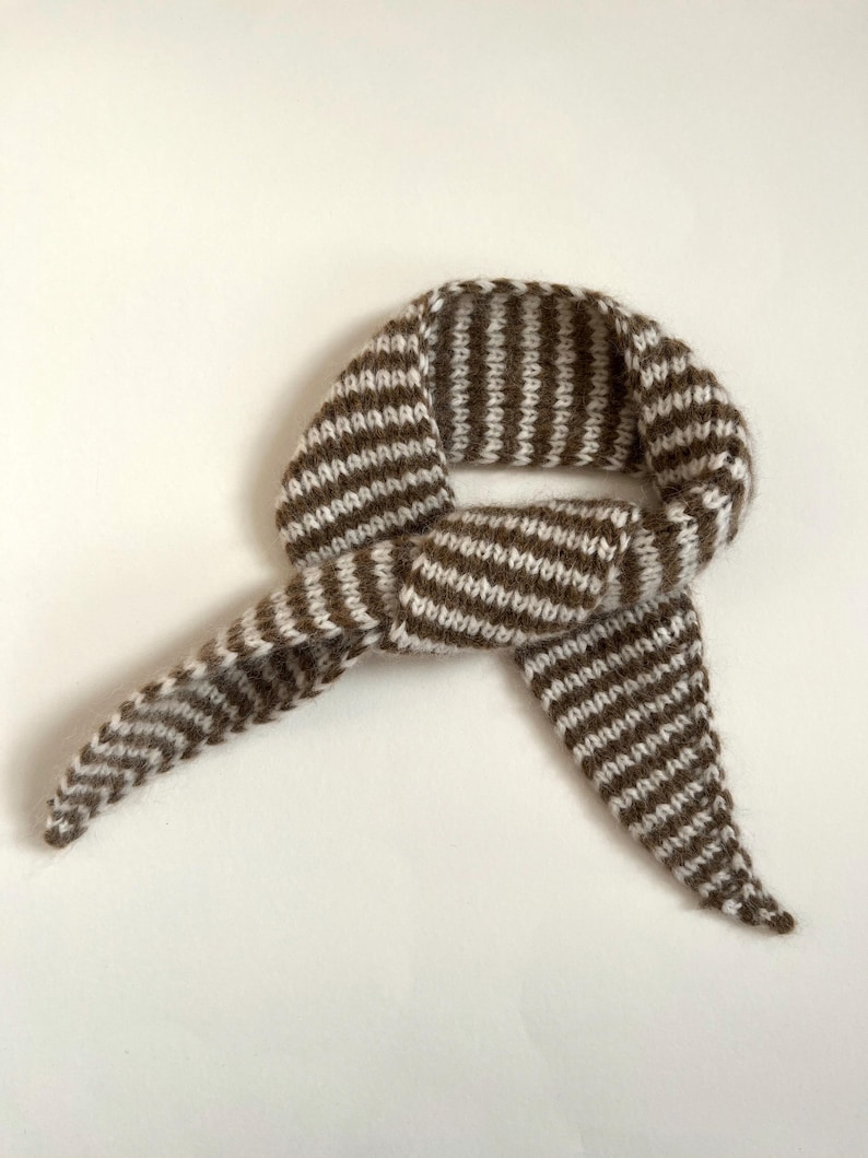 May include: A brown and white striped knitted scarf, knotted in the center. The scarf is made of a soft, textured yarn and has a simple, classic design. The scarf is displayed on a white background.