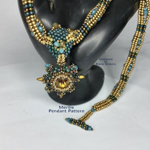 以下が含まれることがあります： 金色と青色のビーズネックレスで、星型のペンダントには大きな透明なクリスタルが飾られています。ペンダントには「Merille Pendant Pattern」と「Designed by Riana Olckers」のラベルが付いています。