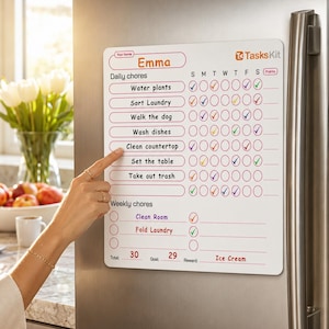 May include: A white magnetic chore chart with the name "Emma" at the top. The chart lists daily and weekly chores with check boxes. The chart is on a refrigerator. A hand is pointing at the "Clean countertop" chore.