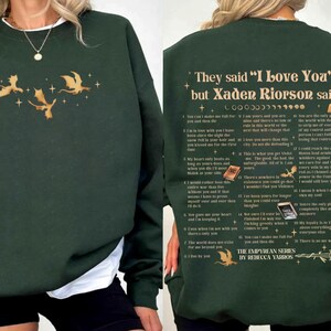 May include: Dark green sweatshirt with gold dragon and star graphics. The front features three dragons and stars. The back has text that reads "They said 'I Love You' but Xaden Riorson said..." with a list of quotes. The Empyrean Series by Rebecca Yarros.