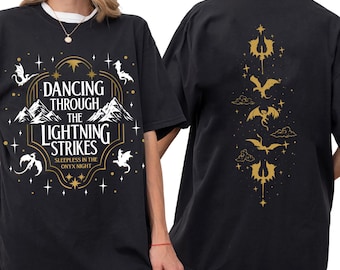 May include: Black t-shirt with a gold graphic on the front and back. The front design features text that reads "Dancing Through The Lightning Strikes" with mountain and dragon illustrations. The back has a vertical dragon design.