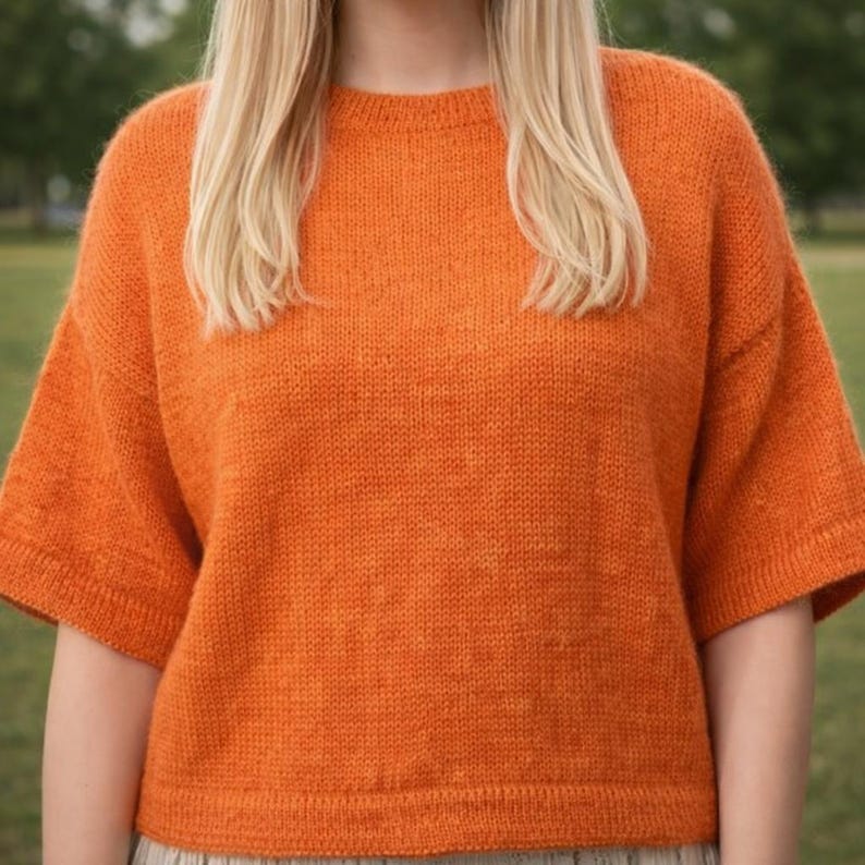 May include: An orange short-sleeved sweater with a crew neck. The sweater is made of a knitted material and has a slightly oversized fit. The sleeves are a shorter length, and the overall style is casual and comfortable.