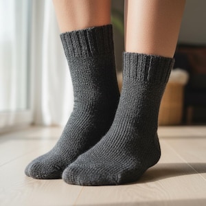 May include: A pair of dark gray, ribbed knit socks. The socks are worn on a person's feet, with the ribbed texture visible on the leg and foot portions. The socks are made of a soft, warm material.