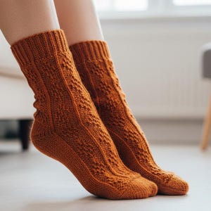 May include: A pair of orange knitted socks with a textured pattern. The socks are pulled up to mid-calf and are resting on a light-colored surface. The socks are a warm, earthy tone.