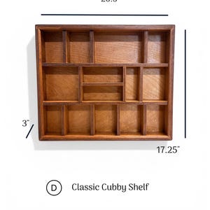 May include: A rectangular wooden cubby shelf with multiple compartments of varying sizes. The shelf measures 20.5 inches in width, 17.25 inches in height, and 3 inches in depth. The text D Classic Cubby Shelf is visible below the shelf.