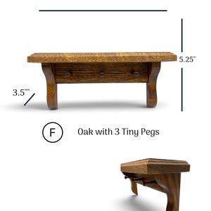 May include: A brown oak wall shelf featuring three small pegs. The shelf measures 12 inches in width, 5.25 inches in height, and 3.5 inches in depth. The text F Oak with 3 Tiny Pegs is displayed below the shelf, which is shown from front and side angles.