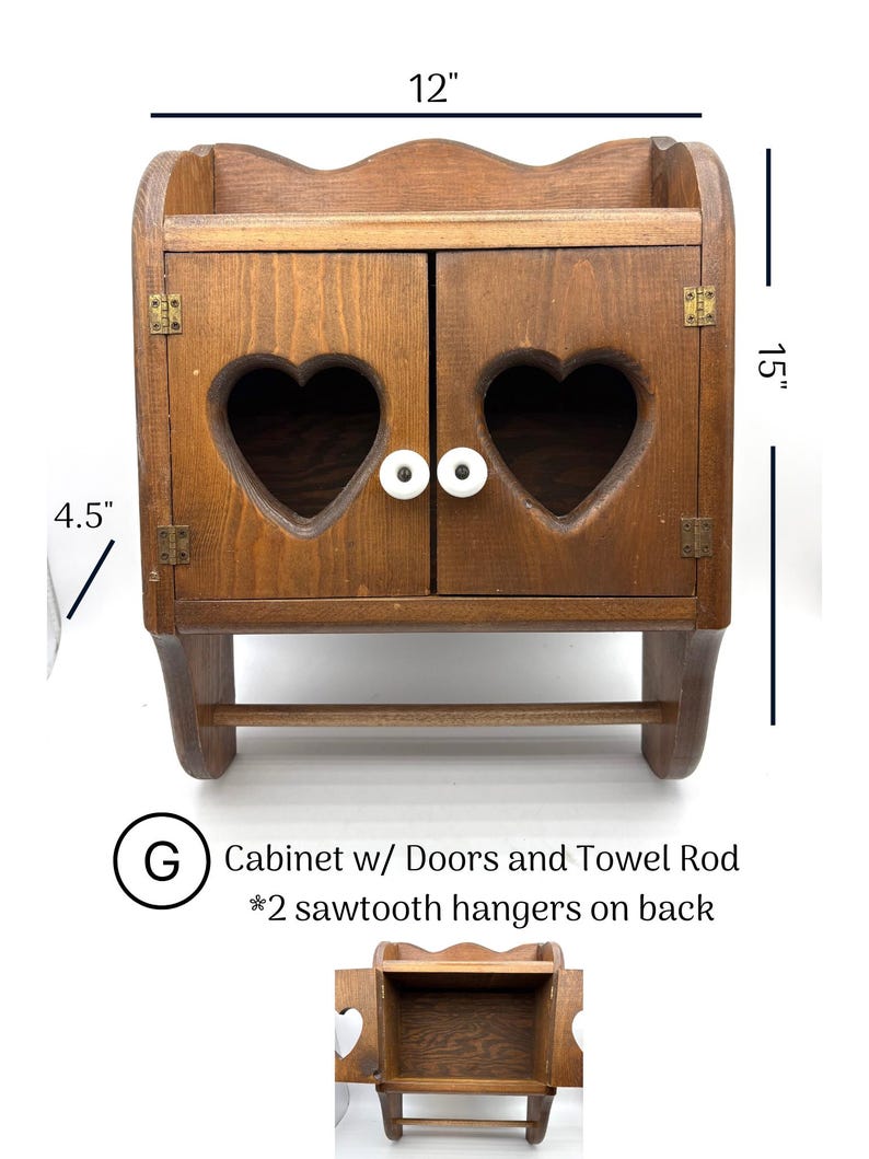 May include: A brown wooden wall cabinet with two doors featuring heart-shaped cutouts and white knobs. It includes a towel rod at the bottom and measures 12 inches wide, 15 inches high, and 4.5 inches deep. Text reads: G Cabinet w/ Doors and Towel Rod.