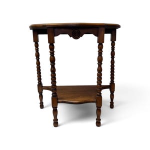 May include: A brown wooden side table featuring a circular top and a lower triangular shelf. The table is supported by four legs with a turned, spindle-style design. A decorative carved circular detail is centered on the front apron.