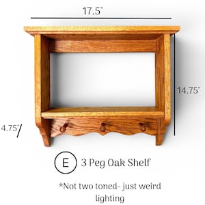 May include: A wooden wall shelf with three pegs, featuring a top shelf and a lower shelf. The unit measures 17.5 inches wide, 14.75 inches high, and 4.75 inches deep. Text on the image reads: E 3 Peg Oak Shelf *Not two toned- just weird lighting.