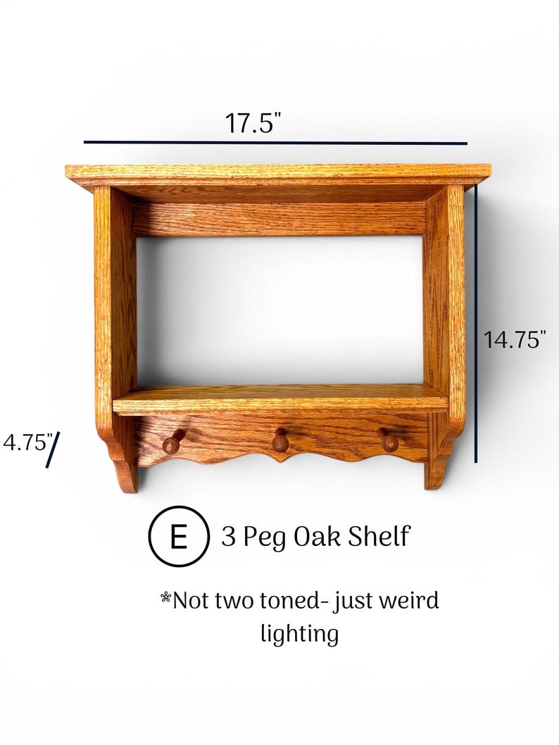 May include: A wooden wall shelf with three pegs, featuring a top shelf and a lower shelf. The unit measures 17.5 inches wide, 14.75 inches high, and 4.75 inches deep. Text on the image reads: E 3 Peg Oak Shelf *Not two toned- just weird lighting.
